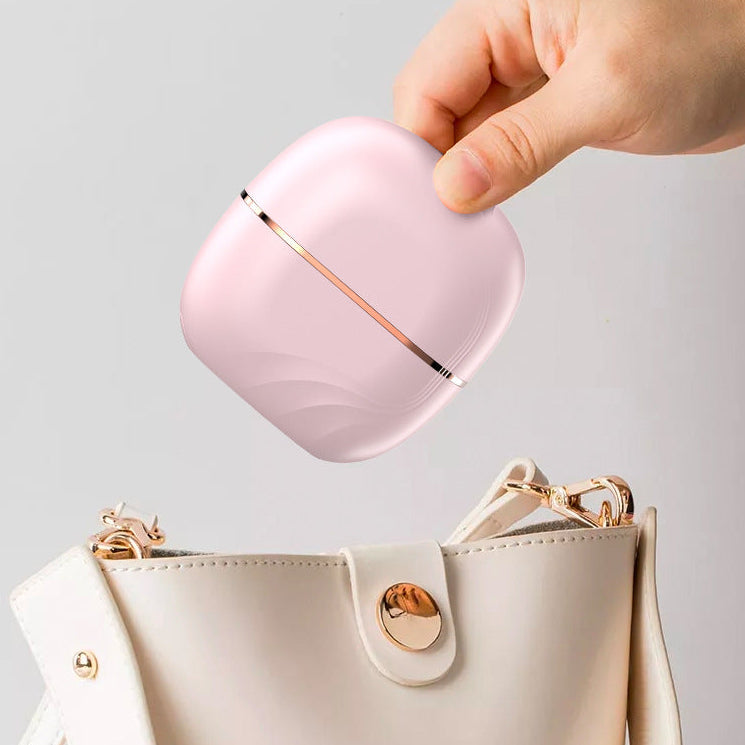 Portable Mini Straightening Comb being put into a bag with a 'click' mechanism, shown with a hand holding it above a beige handbag.